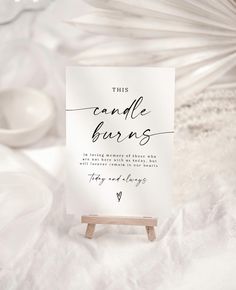 this candle burns sign is on an easel with white linens in the background