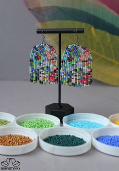 the beaded earrings are on display next to bowls of colored seed beads and a leaf