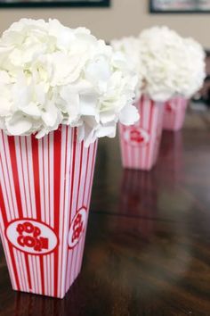 three red and white striped popcorn buckets with flowers in them on a wooden table