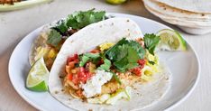 two tacos on a white plate with limes