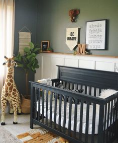 a baby crib with a giraffe stuffed animal in the corner and pictures on the wall