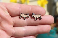 a person is holding two small sheep studs in their left hand and they are both wearing earrings