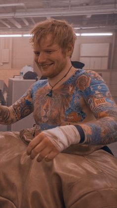 a man with tattoos on his arm sitting in a chair