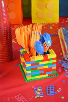 colorful plastic utensils in a lego block holder on a red tablecloth with confetti