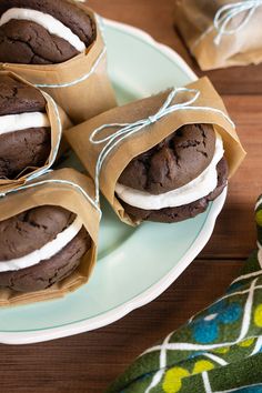 three chocolate cookies wrapped in brown paper on a plate with a green and white napkin