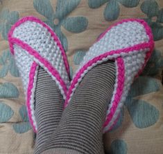 someone's feet with pink and white knitted socks laying on top of a bed