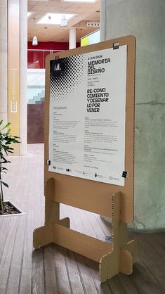 a sign in the middle of a wooden floor next to a plant and potted tree