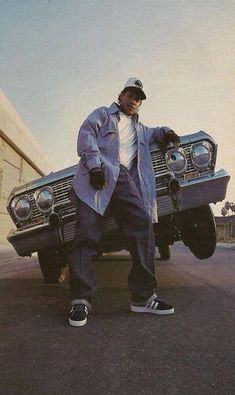 a man standing in front of a car with his hand on the hood and wearing sneakers