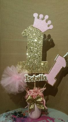 a pink and gold 1st birthday cake topper with the number one on it's base