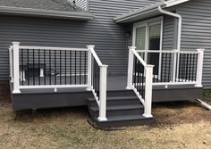 a house with grey siding and white railings on the front porch, next to a black dog