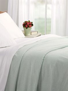 a bed with white linens and a green plant in a pot on the side