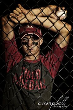 a man holding a baseball behind a chain link fence with his hands on his head