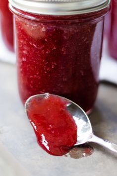 a spoon full of red liquid sitting on top of a table next to a jar