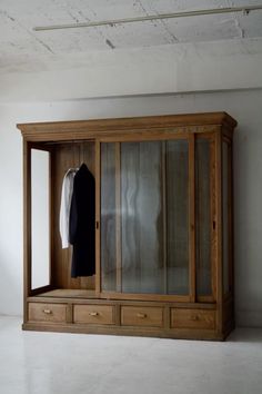 an empty room with a wooden cabinet and clothes hanging on the door, in front of a white wall