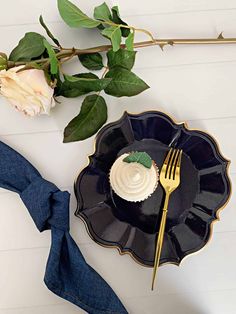 a black plate with a white frosted cupcake on it next to a fork