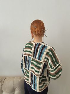 a woman standing in front of a white wall wearing a sweater with multicolored stripes