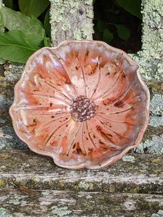 a pink flower shaped bowl sitting on top of a wooden bench next to green leaves