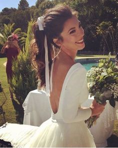 a woman in a white dress holding flowers and smiling at the camera while standing next to a pool