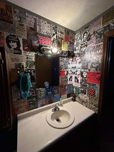 a bathroom sink sitting under a mirror covered in posters