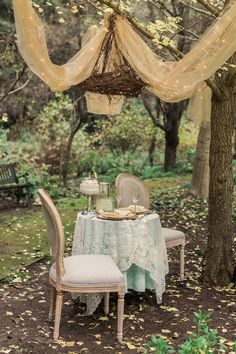 a table set for two under a canopy in the woods