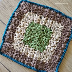 a crocheted square with a green center on a wooden surface, in the shape of a flower