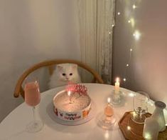 a white cat sitting on top of a table next to a cake and wine glasses