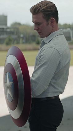 a man holding a captain america shield in his right hand and looking down at the ground