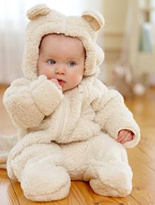 a baby in a teddy bear costume sitting on the floor with his hands to his mouth