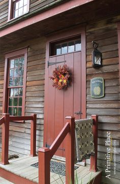 a red door with a wreath on the side of it next to a wooden porch