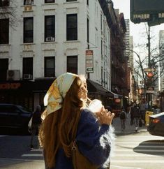 a woman standing on the side of a road next to tall buildings and traffic lights