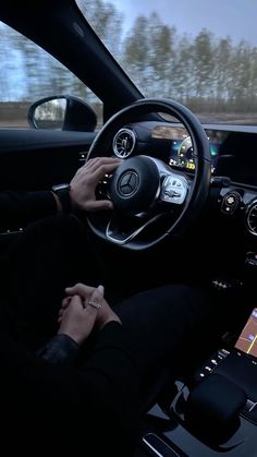 a person driving a car with their hands on the steering wheel, while using an electronic device