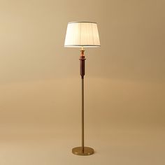 a floor lamp with a white shade on the top and a brown pole underneath it