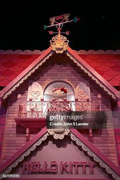 a pink building with a teddy bear on the balcony and red roof at night stock photo