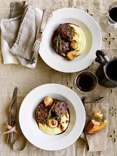 two white plates topped with meat and potatoes next to a cup of coffee on top of a table