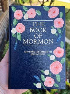 the book of mormon is held up in front of a house with flowers painted on it