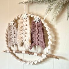 three crocheted ornaments hanging from a branch with snowflakes on it, one is pink and the other is white