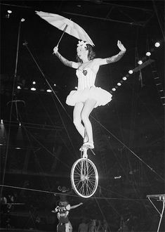 a woman is balancing on a unicycle while holding an umbrella over her head