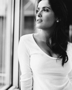 a black and white photo of a woman leaning against a window