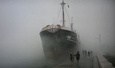 two people walking towards a large ship in the fog