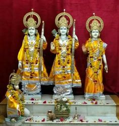 three statues of hindu deities on display in front of a red curtain