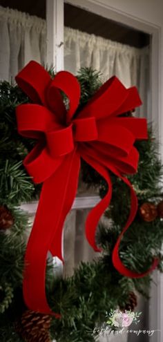 a christmas wreath with a red bow hanging from the side of a window sill