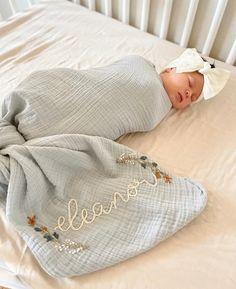 a baby wrapped in a blanket laying on top of a crib next to a pillow