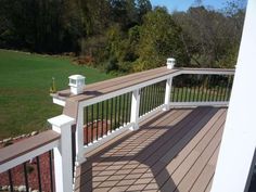 a deck with white railings and wood flooring next to a grassy area in the background