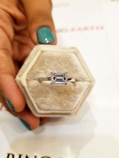 a woman's hand holding an engagement ring in a velvet box with a diamond on it