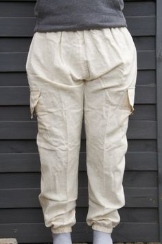 a person standing in front of a black wall wearing white pants and gray socks with one foot on the ground