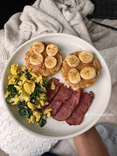 a white plate topped with breakfast foods on top of a bed next to a person