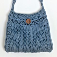 a blue crocheted purse with a button on the front and side pocket, sitting on a white surface