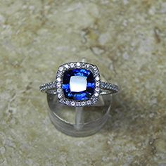 an engagement ring with a blue stone surrounded by white diamonds on a marble surface,