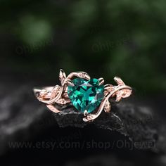 a green heart shaped ring sitting on top of a piece of black rock with leaves around it