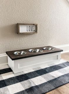 a dog bed with two bowls on top and a love sign above it